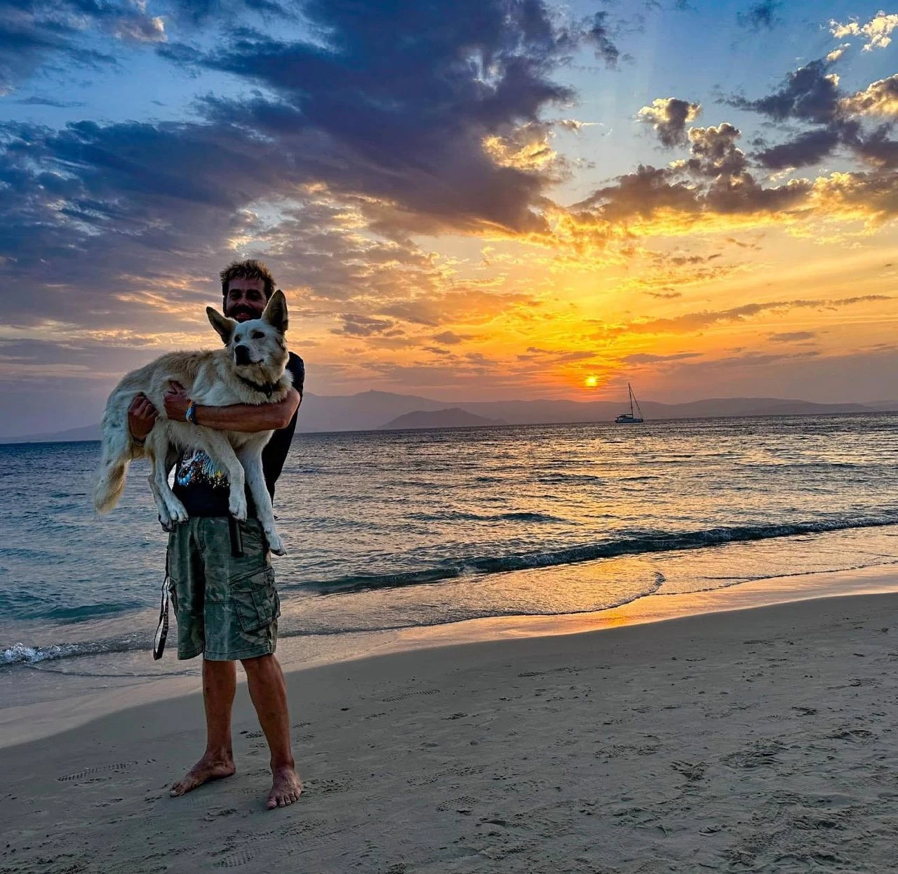 Ondra holding his dog on the beach at sunset